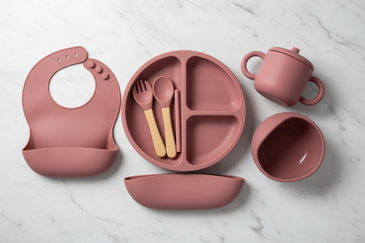 Flat lay of mauve 6-piece silicone dinner set on white marble